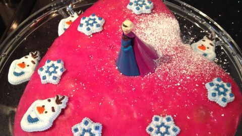 Ein Herz-Zitronenkuchen steht auf einem Glasplatten, dekoriert mit Schneeflocken und Figuren, umgeben von einer eleganten Küche.