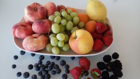 Eine Schale enthält eine Vielfalt an frischem Obst wie Pfirsiche und Trauben, umgeben von Erdbeeren, Blaubeeren und Brombeeren.