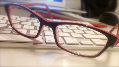 Eine Brille liegt auf einem Schreibtisch neben einer Computer-Tastatur, bereit zum Reinigen für bessere Sicht.