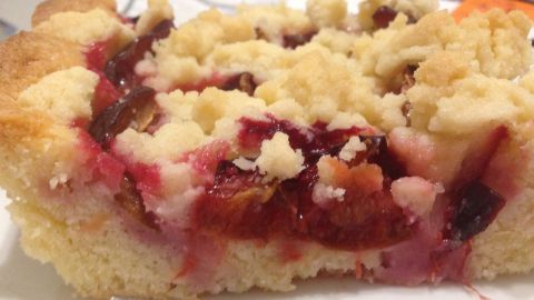 Ein saftiges Stück Pflaumenkuchen mit Butterstreuseln liegt auf einem Teller und wird genossen.