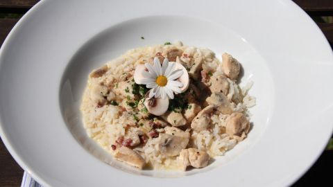 Ein Sahneschnitzel liegt auf einem weißen Teller, umgeben von cremiger Zwiebelsuppe und garniert mit einer Blume.