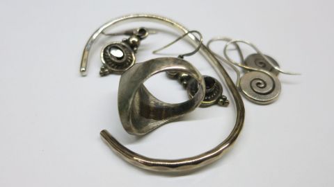 Angelaufenen Silberschmuck mit Bier reinigen: Reinigt besser als jedes teure Putzmittel. Ein glänzendes Schmuckstück liegt auf einem weißen Untergrund, während Bier zur Reinigung benutzt wird.