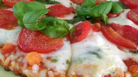 Eine Mozzarella Tiefkühlpizza mit frischen Tomaten und Basilikum wird appetitlich auf einem Teller serviert.