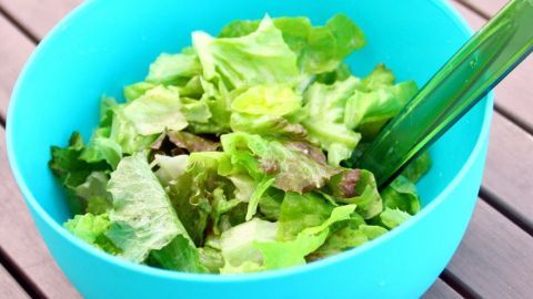 Ein blauer Schüssel befindet sich auf einem Holztisch, gefüllt mit frischem, grünem Salat, bereit für die Salatsoße.