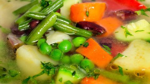 Eine bunte Gemüsesuppe wird in einem Topf erhitzt, sie enthält grüne Bohnen, Karotten und Erbsen, ideal zum Würfelförmigen Einfrieren.