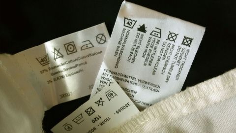 Auf einem weißen Stoff sind mehrere Wäscheetiketten sichtbar, die Pflegehinweise zum Wäschewaschen anzeigen.
