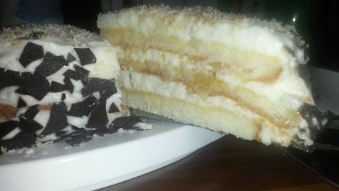 Ein Abschnitt einer Ananas-Kokos-Torte auf Teller zeigt luftige Schichten mit Sahne und Ananas, garniert mit dunklen Schokostückchen.