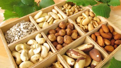 Nüsse und Samen liegen sortiert in einer Holzkiste, begleitet von grünen Blättern, könnten Serotoninmangel vorbeugen.