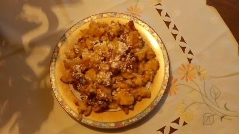 Auf einem schön dekorierten Tisch liegt ein Teller mit Quark-Apfel-Schmarrn, der mit Puderzucker bestreut ist.