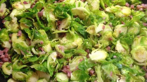 In einer großen Pfanne wird frischer Speckrosenkohl mit kleinen Stückchen Speck zubereitet, um eine herzhafte Pasta zuzubereiten.