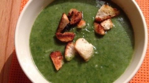 Eine grüne Spinatsuppe mit knusprigen Knoblauchcroutons in einer Schüssel, auf einem orangefarbenen Tischset.