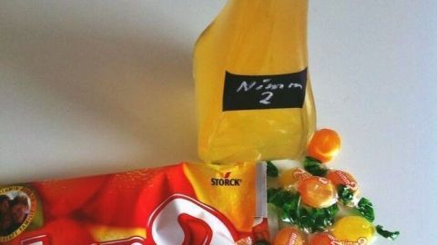 Eine gelbe Likörflasche mit "Nimm 2" daneben, umgeben von Nimm 2 Bonbons aus einer aufgerissenen Packung auf einem Tisch.