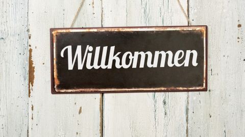 Ein nostalgisches Blechschild mit dem Schriftzug „Willkommen“ hängt an einer rustikalen Holzwand.