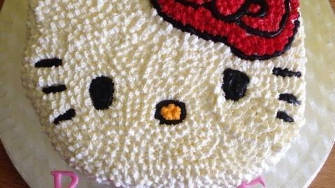 Ein "Hello Kitty" Kuchen liegt auf einem Tisch, zeigt das Gesicht der Figur mit roter Schleife. Text: "4 ROSIE".