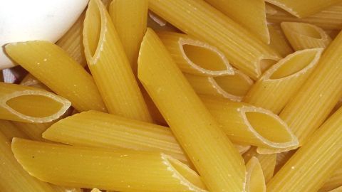 Penne-Nudeln liegen neben Eiern und einer Zwiebel, ideal für Vorratshaltung in der Küche.