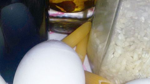 Eier liegen auf Penne-Nudeln, eingerahmt von Ölflasche und Reisedose auf einem Küchentuch.