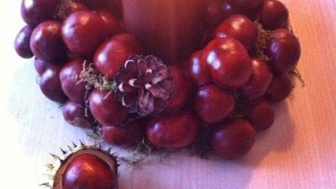 Ein Kastanien-Kerzenkranz aus glänzenden Kastanien umgibt eine brennende Kerze und steht auf einem hellen Untergrund.
