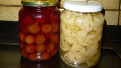 Drei Gläser mit eingekochtem Obst stehen auf einer dunklen Fläche. Fruchtkonserven in verschiedenen Farben sind sichtbar.