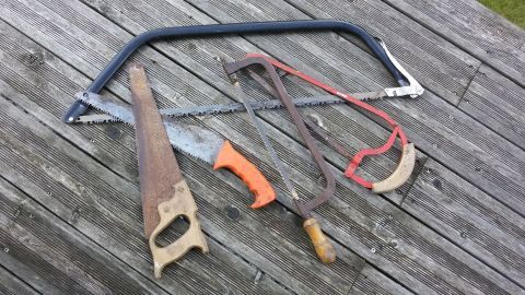 Eine Handsäge, eine Bügelsäge und weitere Werkzeuge liegen auf einem Holzuntergrund, bereit zum Sägen im Heimwerkerkontext.