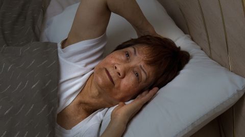 Eine ältere Frau liegt im Bett und hält sich die Ohren zu, während sie Schwierigkeiten hat, aufgrund von Schlafstörungen zu schlafen.