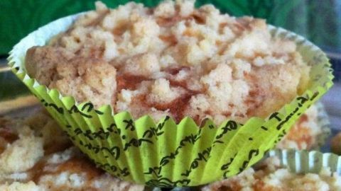 Goldene Apfel-Zimt Muffins mit Streuseln stehen auf einem Teller, umgeben von einem bunten, gemusterten Hintergrund.