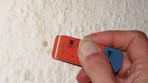 Ein Radiergummi entfernt Flecken von einer strukturierten weißen Wand, während eine Hand den Radiergummi hält.