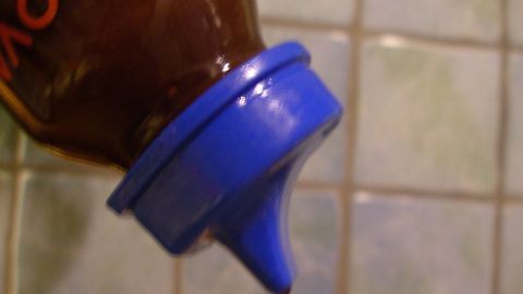 Ein Babyfläschchen wird über einer Fliese gehalten, während es Salatdressing auf einen Teller verteilt.