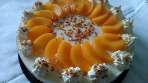 Eine Käsetorte mit Pfirsichscheiben und Sahnehäubchen dekoriert, präsentiert auf einem weißen Untergrund.