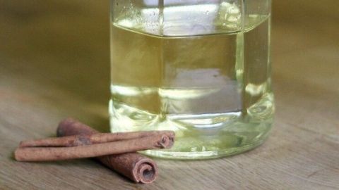 Eine Glasflasche mit Zimtöl steht auf einem Holztisch, umgeben von Zimtstangen vor grünem Hintergrund.