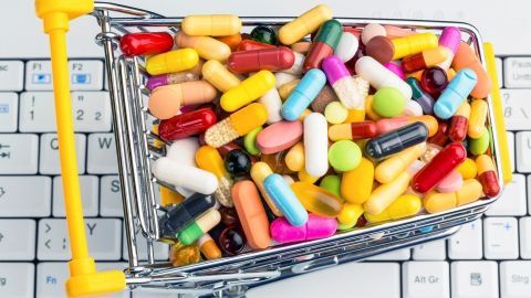 Ein Einkaufswagen voller bunter Medikamente steht auf einer Computertastatur, was das Online-Kaufen von rezeptfreien Medikamenten symbolisiert.