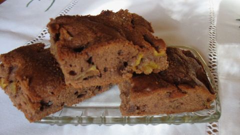 Ein saftiger Apfel-Kakao-Kuchen liegt auf einem Glasteller, umgeben von einem weißen Tischcloth und strahlt eine einladende Wärme aus.