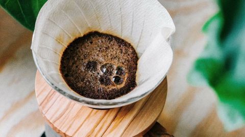 Ein Kaffeefilter mit Kaffeesatz steht auf einem Holztisch, während Wasser durch den Satz läuft, um frisch gebrühten Kaffee zu erzeugen.