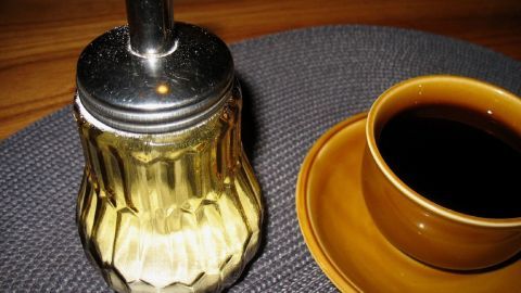 Ein gläserner Kaffeeweißer steht auf einem Tisch neben einer Tasse Kaffee, bereit zum portionieren.