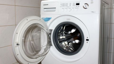 Eine Waschmaschine mit offener Tür steht in einem gefliesten Raum und wartet darauf, Wäsche zu waschen.