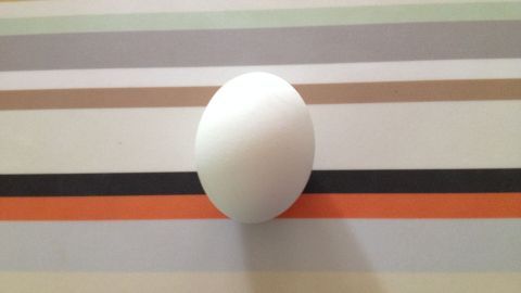 Ein weißes Ei liegt ruhig auf einer bunten, horizontal gestreiften Oberfläche.