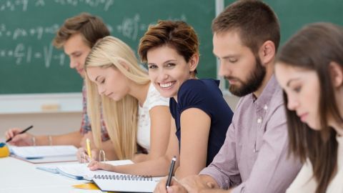 Eine Gruppe von Studenten sitzt an einer langen Tafel, konzentriert am Lernen und Notizen machen in einem Klassenzimmer.