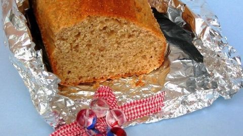 Ein Brotkuchen aus Dinkelgrieß liegt auf metallischer Folie, dekoriert mit einer bunten Schleife, vor einem blauen Hintergrund.