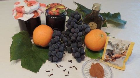 Auf einem weißen Tisch liegen Trauben und Orangen zusammen mit Marmeladengläsern, Gewürzen und Blättern.