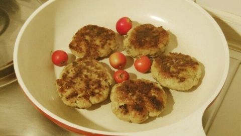 Puten-Frikadellen braten in einer Pfanne, umgeben von kleinen roten Tomaten, in einer modernen Küche.