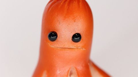 Ein lustiges, kunstvoll gestaltetes Würstchen in Form eines kleinen Tintenfischs steht aufrecht auf einem weißen Hintergrund.