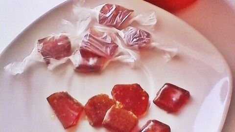 Ein Teller mit selbstgemachten Honig-Minz Bonbons liegt vor einem Glas Honig. Die Bonbons sind glänzend und transparent.