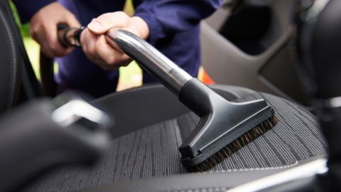 Ein Staubsauger reinigt gerade einen Autositz, während die Person in einem Fahrzeuginterieur steht und staubt.