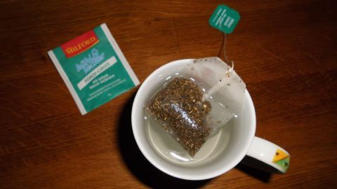 Ein Teebeutel schwebt in einer Tasse mit Wasser, um einen Kaltaufguss herzustellen, auf einem Holztisch.