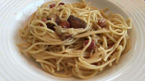 Ein Teller Spaghetti Carbonara ohne Sahne zeigt dampfende, cremige Nudeln mit Speckstücken in einem hellen, klassischen Ambiente.