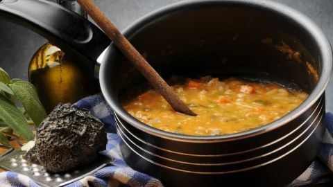 Ein Kochtopf mit dampfender Suppe steht auf einer Arbeitsplatte, während ein Holzlöffel darin umrührt.