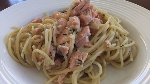 Nudeln mit Lachs liegen appetitlich auf einem weißen Teller, umgeben von einer Holzoberfläche.