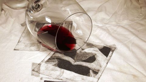 Mit Rasierschaum sogar aus heller Kleidung Rotweinflecken vollständig entfernen. Ein umgekipptes Weinglas mit Rotwein auf einem weißen Tuch hinterlässt Flecken, die entfernt werden sollen.