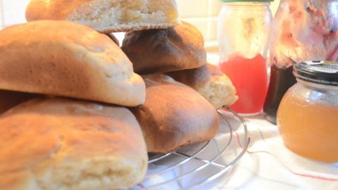 Auf einem Kühlregal liegen frische Milchbrötchen, während Marmelade und Honig in Gläsern daneben stehen.