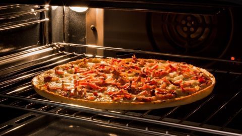 Eine große Pizza wird auf einem Rost in einem Ofen gebacken, um gleichmäßige Hitze und knusprigen Boden zu gewährleisten.
