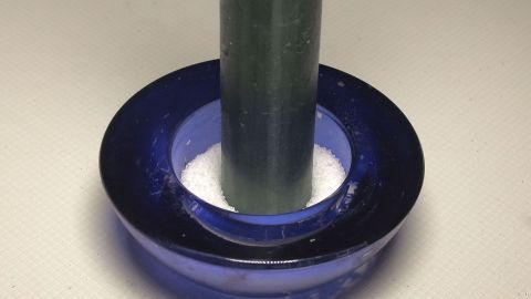 Kerzenwachs aus Kerzengläsern mithilfe von Salz leicht entfernen. Ein blauer Kerzenhalter mit einer grünen Kerze steht darin, umgeben von weißem Salz zur Entfernung von Kerzenwachs.